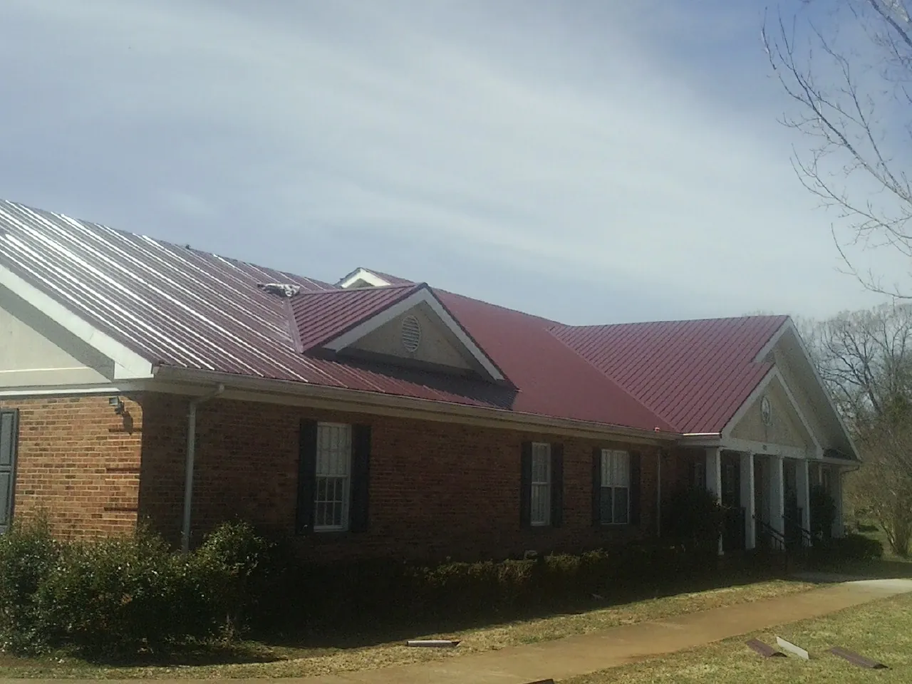 Red metal roof with gabled entries on a long brick building, from a Hail Damage Roof Repair job in Brent