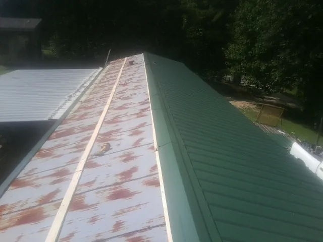 Old rusted panels beside newly installed green metal roofing — Wind Damage Roof Repair by Roofing Brothers in Brent