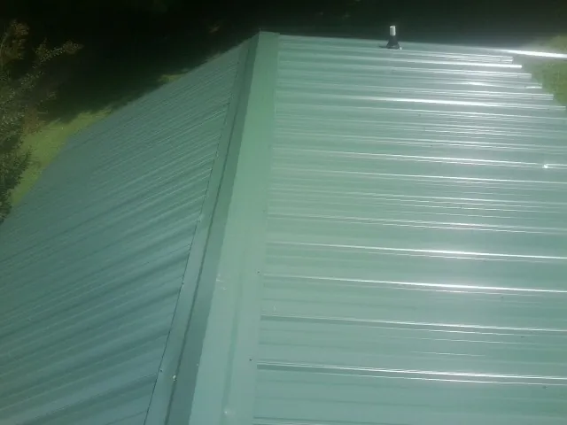 New green metal panels meeting at the ridge of a roof — Flat Roof Repair work by our crew in Brent