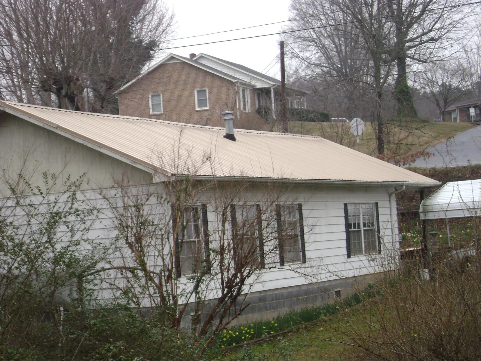 Tan metal roof on a white sided house set into a hillside — Commercial Roofing by Roofing Brothers in Brent