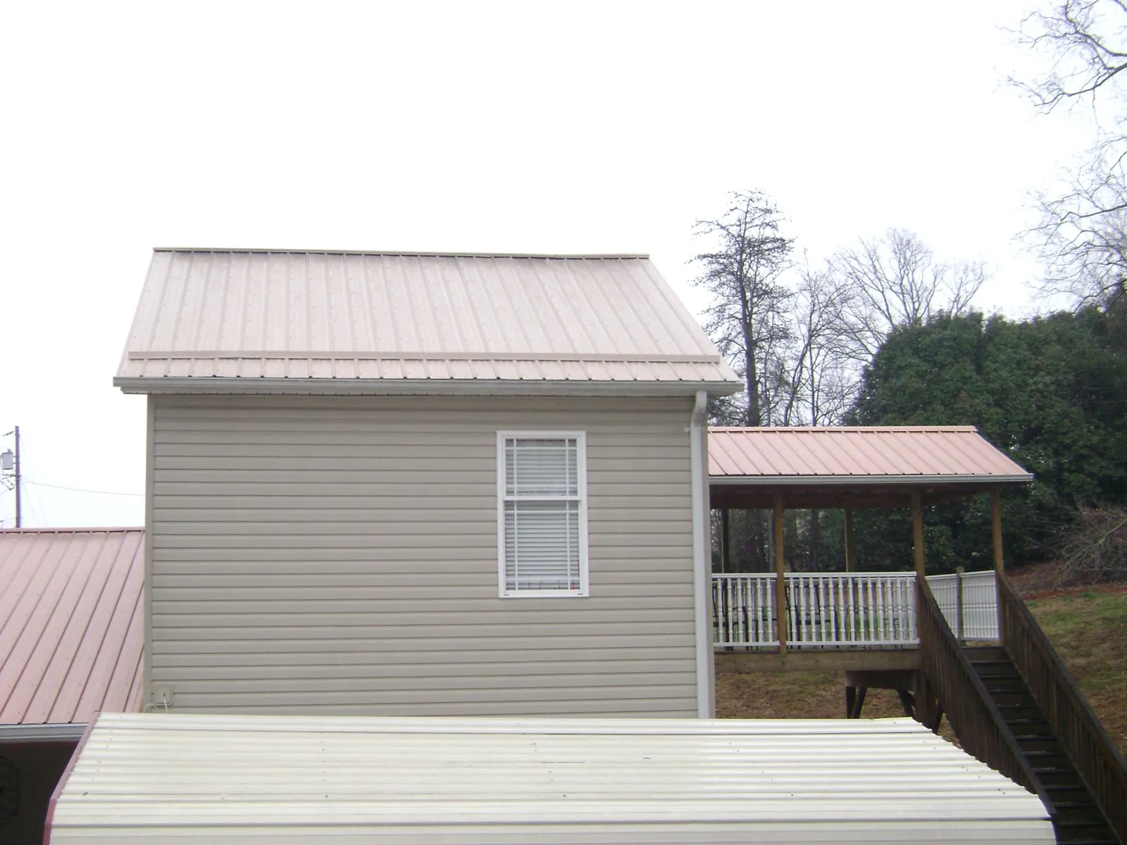 Tan metal roofs on a two story addition and attached porch, from a Roof Replacement job in Brent